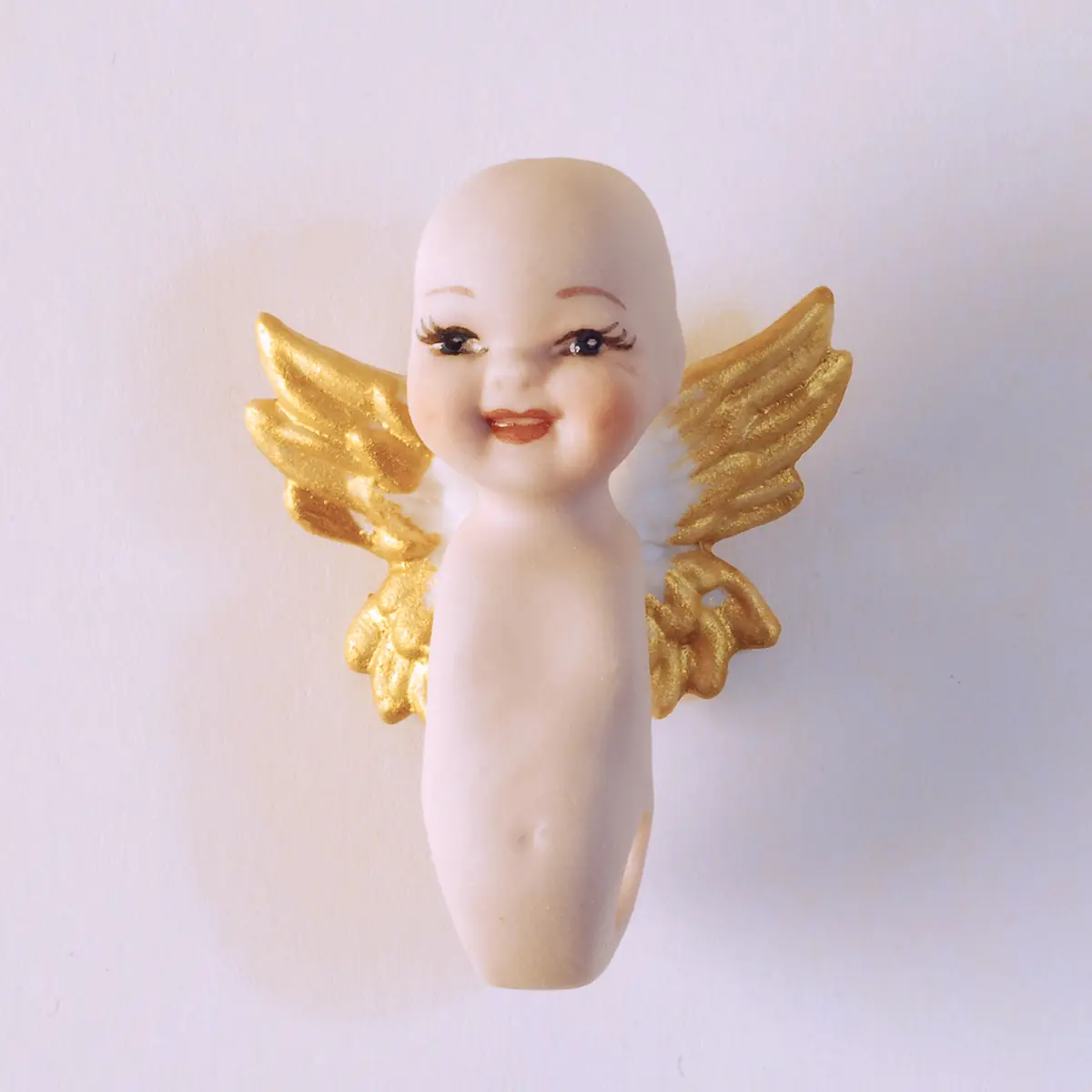 Bambolina in porcellana biscuit raffigurante un piccolo angioletto sorridente con ali bianche e punte dorate.
