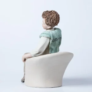 Statua in porcellana di Alan, ragazzo seduto su poltrona bianca con camicia e maglioncino azzurro sulle spalle.