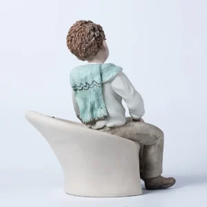 Statua in porcellana di Alan, ragazzo seduto su poltrona bianca con camicia e maglioncino azzurro sulle spalle.