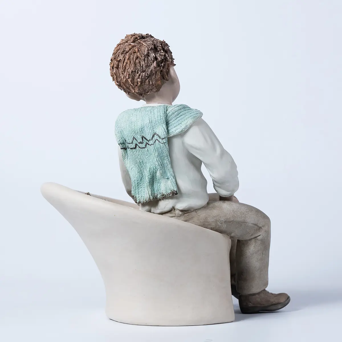 Statua in porcellana di Alan, ragazzo seduto su poltrona bianca con camicia e maglioncino azzurro sulle spalle.