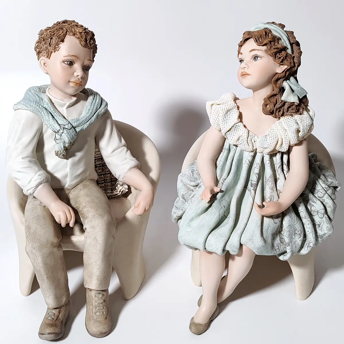 Statuette in porcellana di Alissa e Alan seduti su una poltrona.