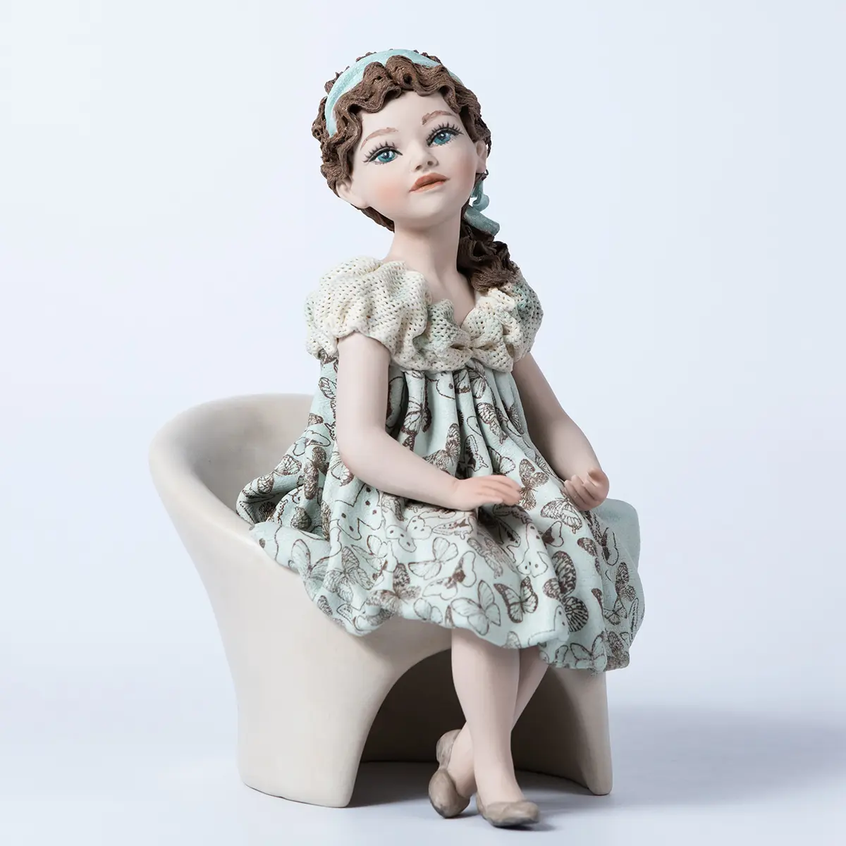 Statua in porcellana di ragazza su poltrona bianca con abito azzurro acquamarina decorato a farfalle e bavero in tulle.