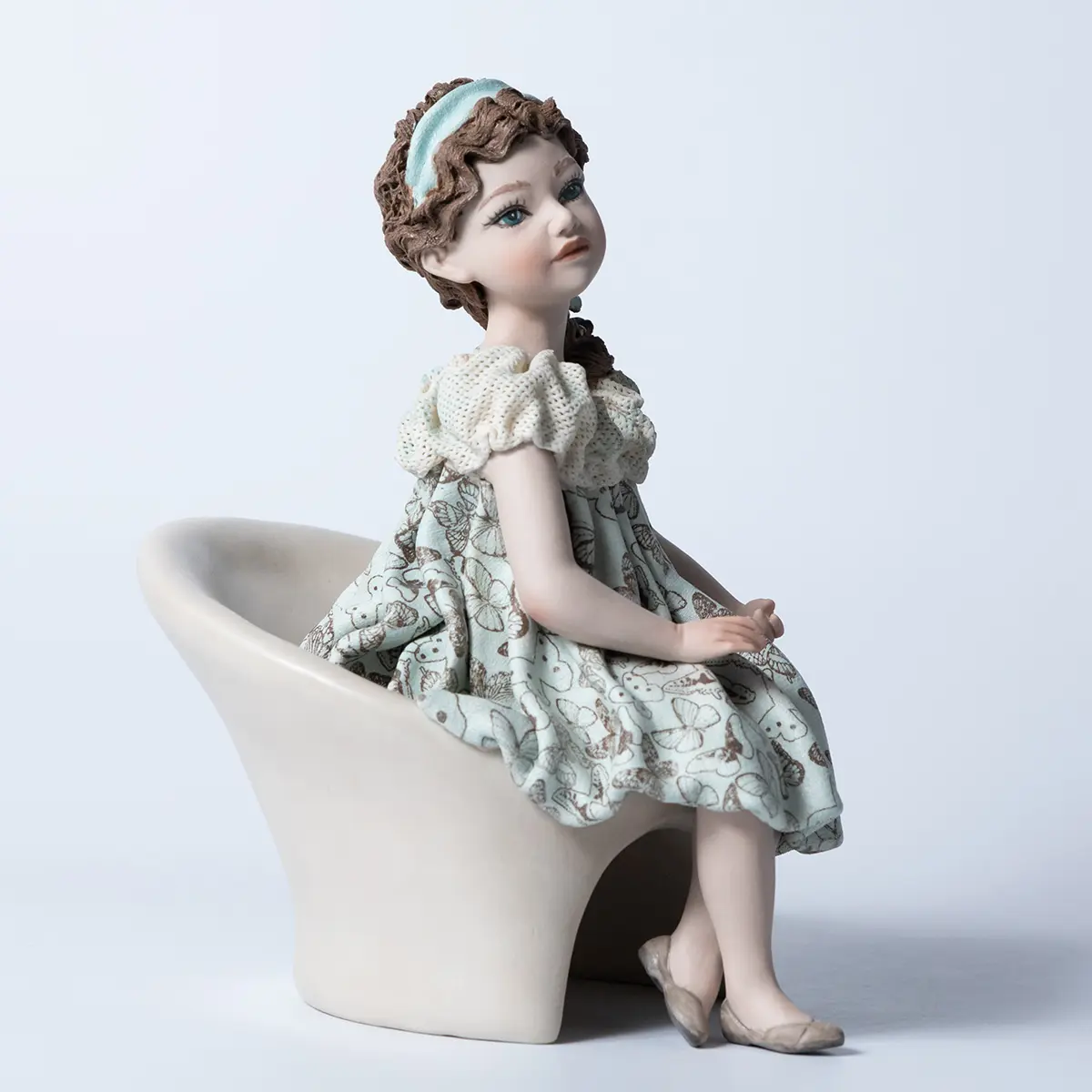 Statua in porcellana di ragazza seduta su poltrona bianca con abito azzurro acquamarina e decoro di farfalle.