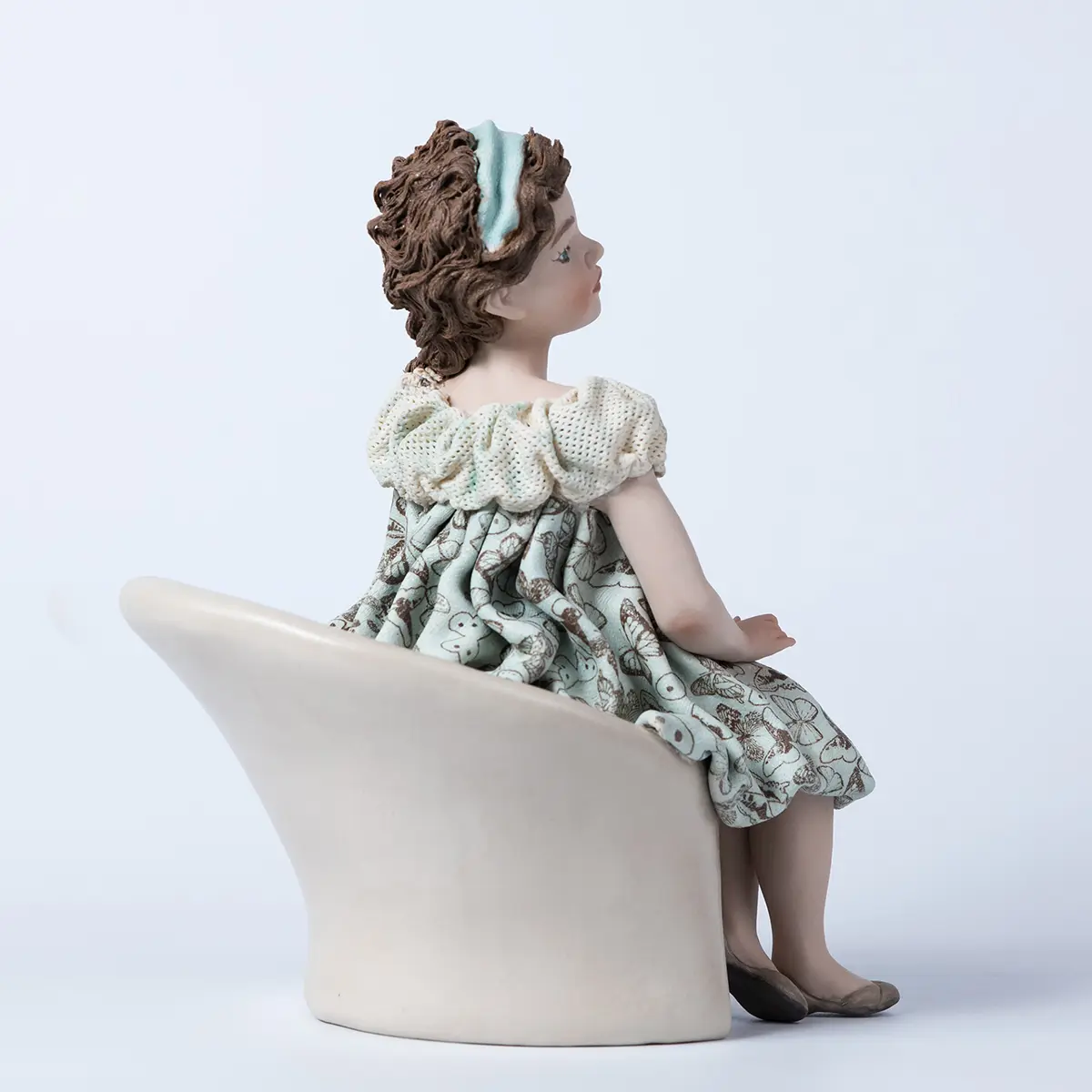 Statua in porcellana Alissa seduta su poltrona bianca con abito azzurro acquamarina a farfalle e bavero in tulle.