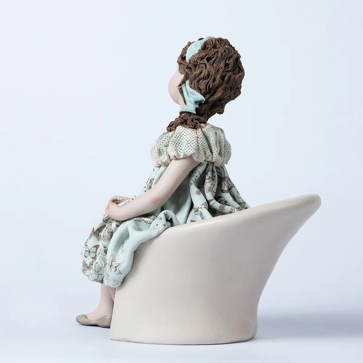 Statua in porcellana di ragazza seduta su poltrona bianca, con abito azzurro acquamarina a farfalle e bavero in tulle.