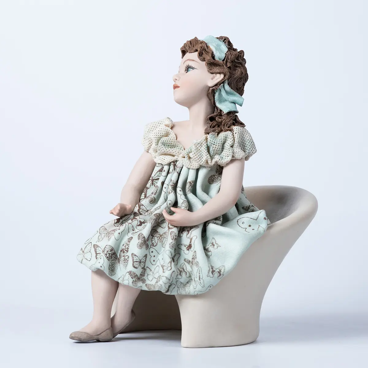 Statua in porcellana Alissa, ragazza seduta su poltrona bianca in abito azzurro acquamarina decorato con farfalle.