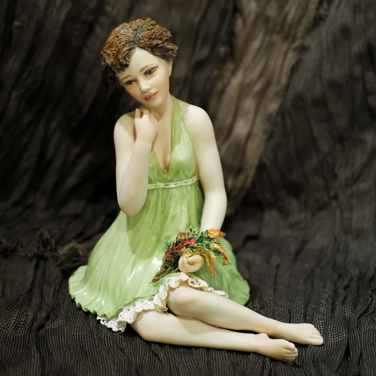 Statua in porcellana con donna seduta, mazzo di fiori, abito verde primavera e sottogonna in pizzo.