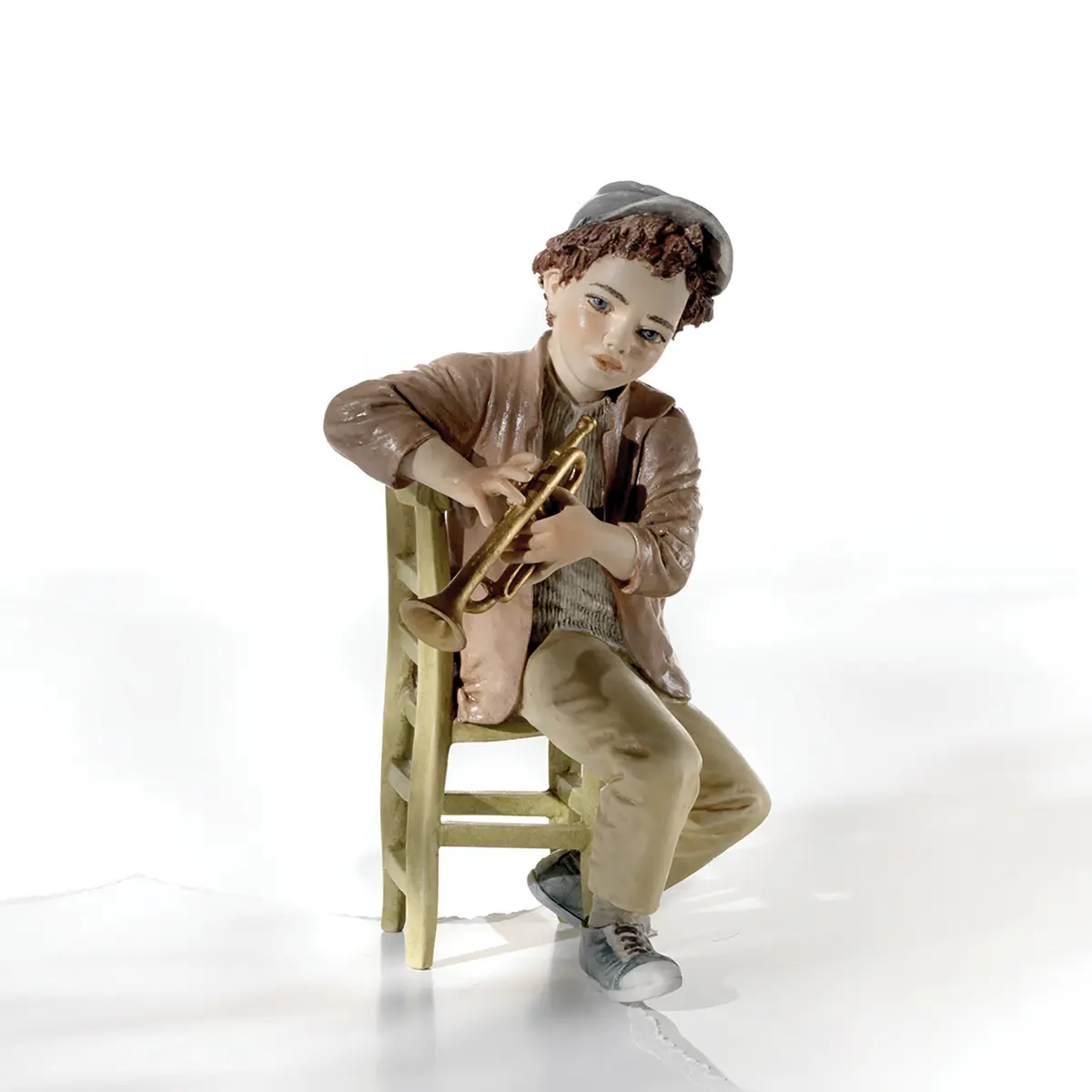 Statua in porcellana di trombettista jazz in giacca nocciola e berretto grigio, seduto su una sedia verde.