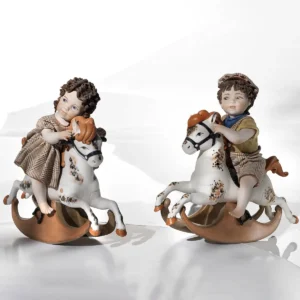 Statue in porcellana Sibania di un bimbo e una bimba su cavallini a dondolo con abiti a quadretti marroni.