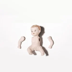 Bambolina in porcellana biscuit seduta a terra con braccia mobili e capelli corti castani.
