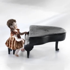 Statua in porcellana di una piccola pianista in abitino rosa che suona un pianoforte a coda nero.