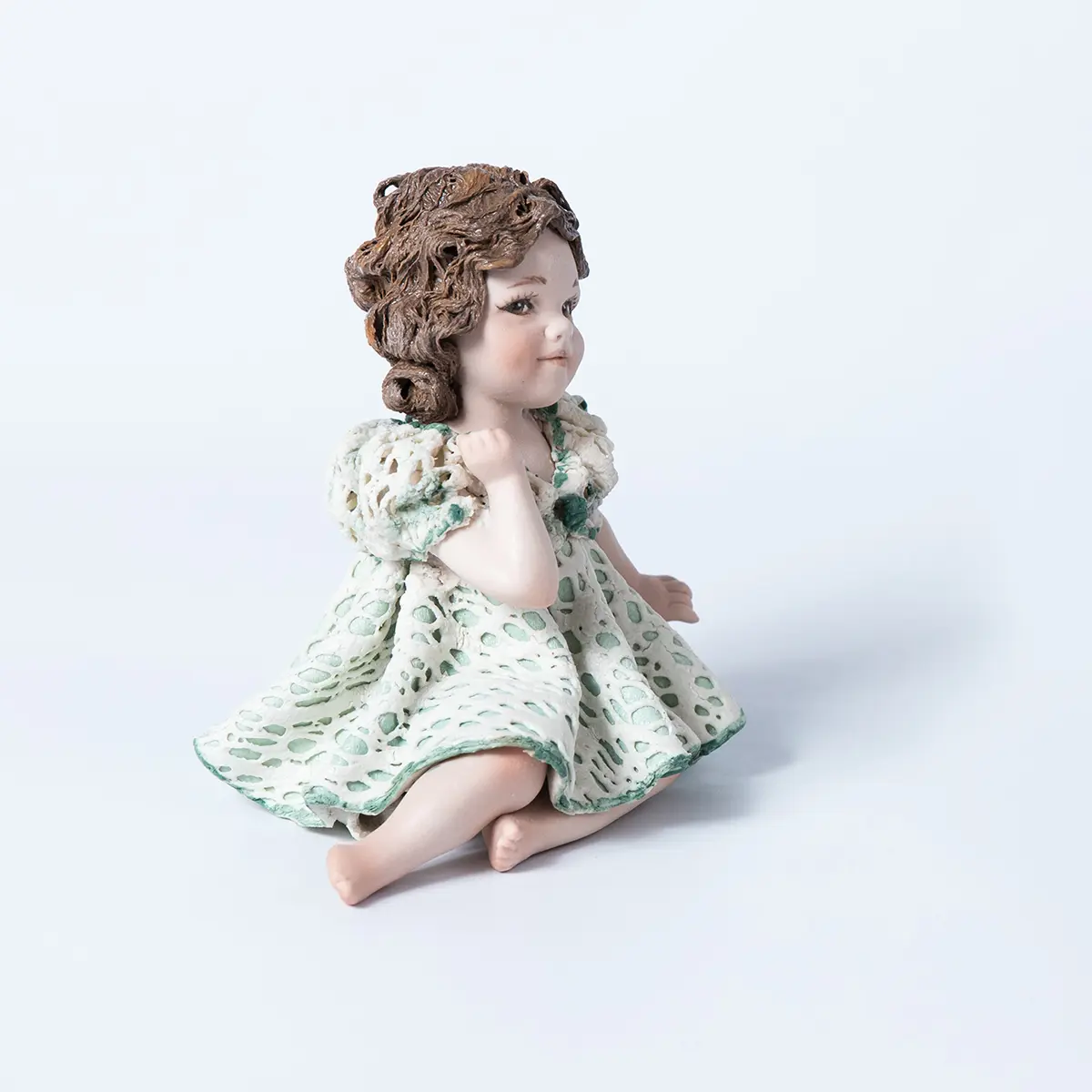 Statua in porcellana di bimba con abito in pizzo bianco e verde, fiocco sul petto e chignon ai lati del collo.