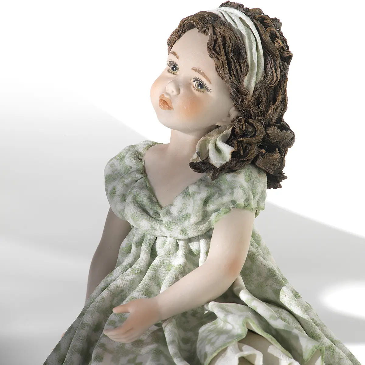 Statua in porcellana di ragazza con abito verde pastello e fascia bianca, seduta su uno scalino marmorizzato.