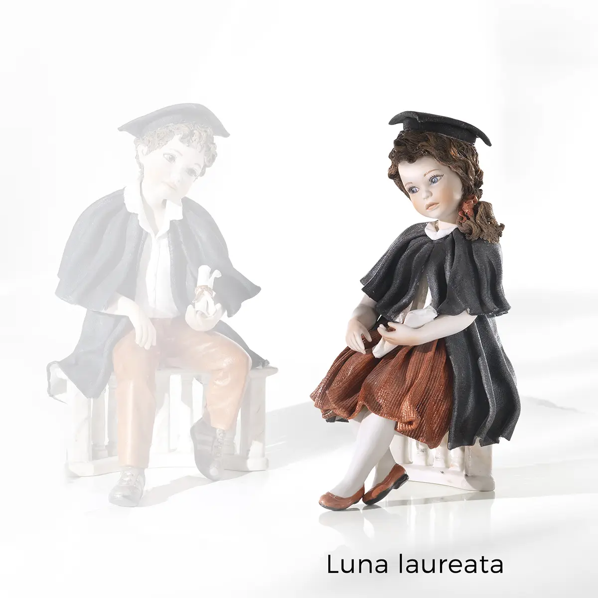 Statua in porcellana di ragazza laureata con toga, tocco nero, gonna rossa e pergamena, seduta su balaustra marmorizzata.