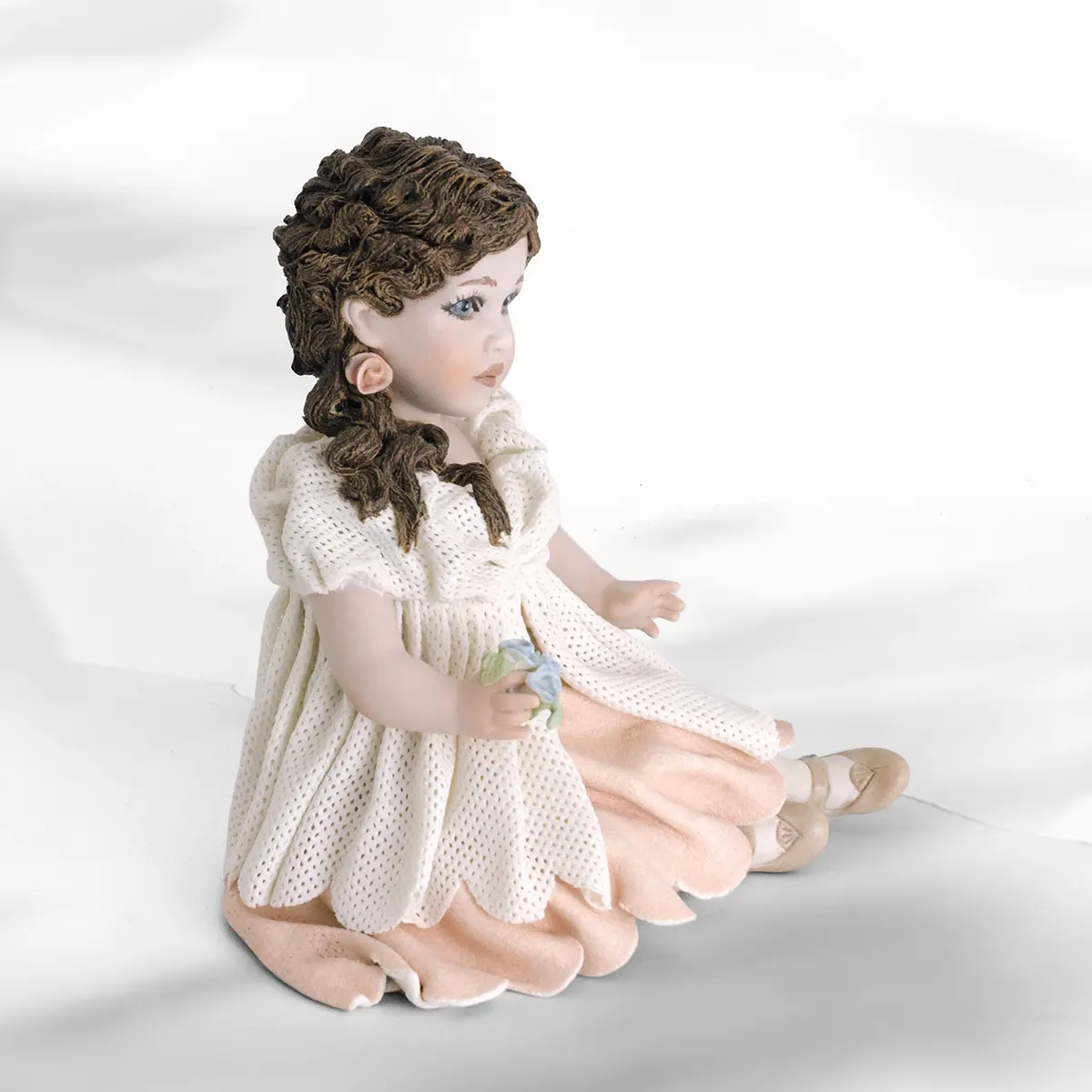 Statua in porcellana di ragazza seduta con abito in tulle, sottogonna rosa, bavero e fiorellini colorati in mano.
