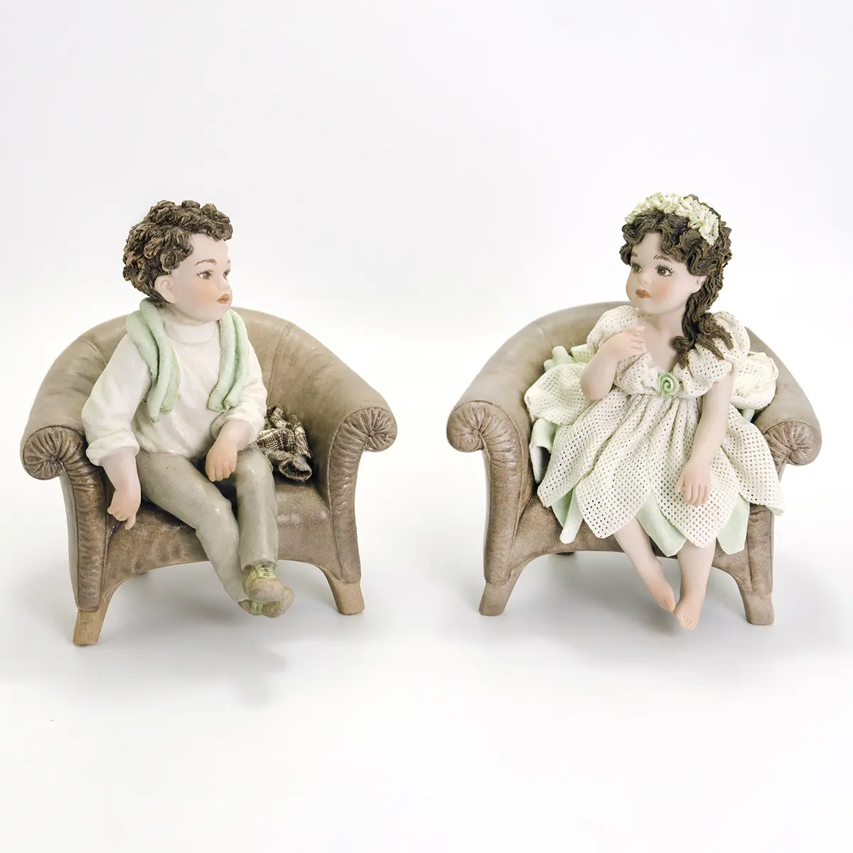 Statue in porcellana Giulio e Giulietta seduti su poltrone: bimbo in maglione e sciarpa verde, bimba in abito di tulle.