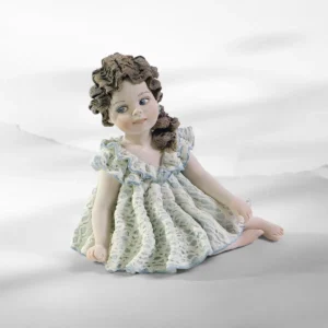 Statua in porcellana di bimba seduta in abito in pizzo bianco e azzurro con coda fermata da una rosellina.