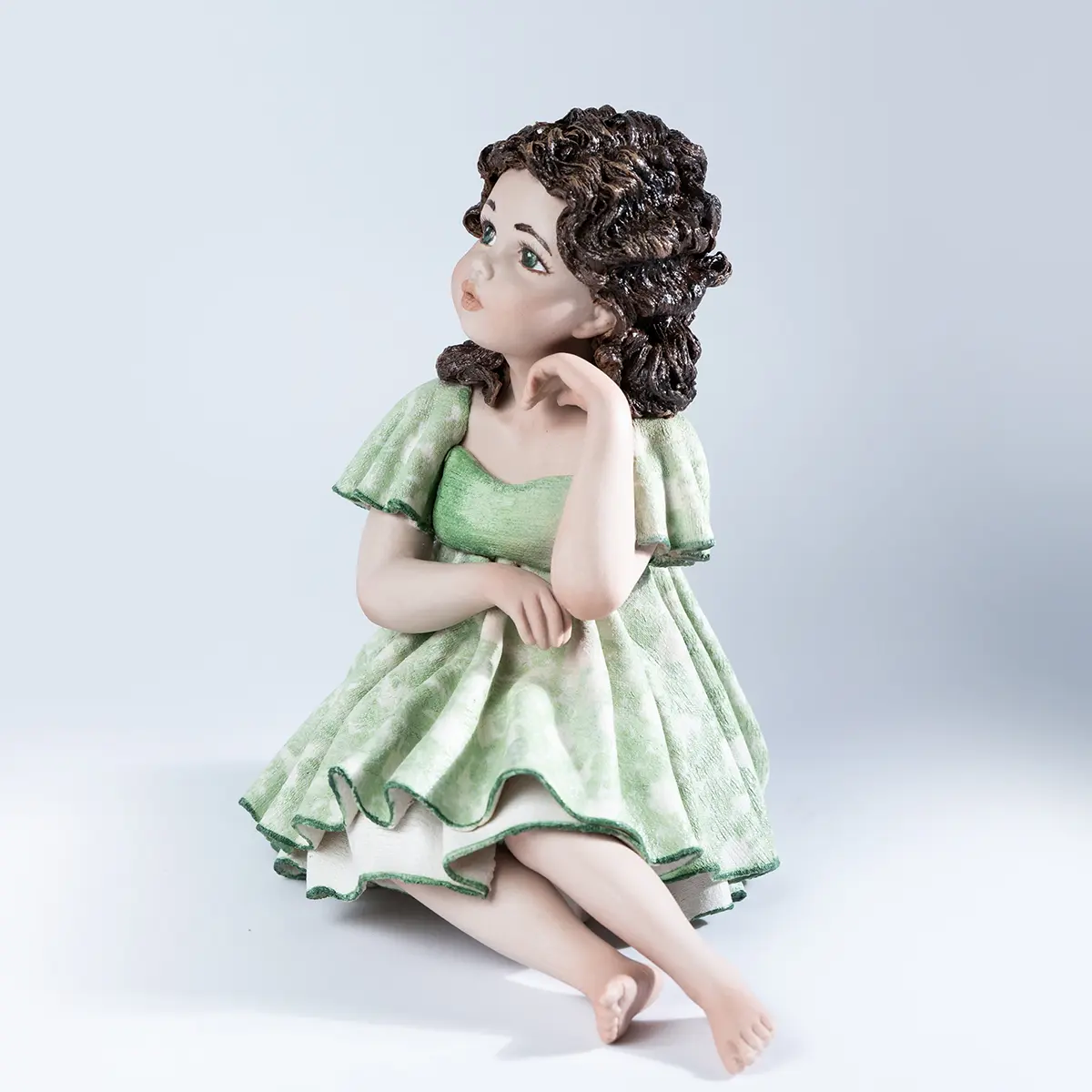 Statua in porcellana di ragazza seduta su sgabello con abito verde tè, bordi verde smeraldo e capelli castani.