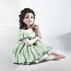 Statua in porcellana di ragazza seduta su sgabello, con abito verde tè, bordi smeraldo e capelli castani sciolti.