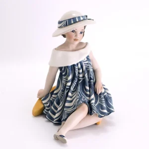 Statua in porcellana Lidia di Sibania 2023 in abito blu navy e bianco, ampio cappello e base a mezzaluna giallo ocra.