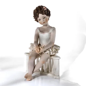 Statua in porcellana con ballerina in tut&ugrave; di pizzo seduta su balaustra marmorizzata e fiocco bianco tra i capelli.