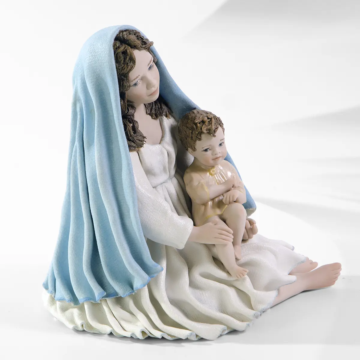 Statua in porcellana della Madonna con Gesù Bambino in braccio, abito bianco, velo azzurro e casacchina crema.