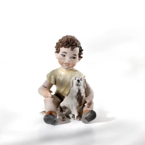Statua in porcellana di un bimbo con cagnolino bianco in braccio, maglietta gialla e pantaloncini marroni.