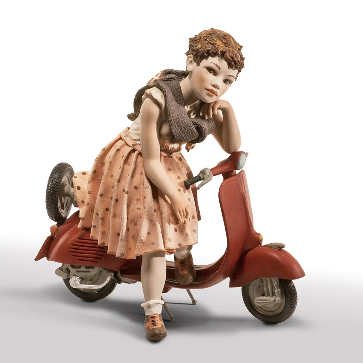 Statua in porcellana di ragazza seduta su Vespa rossa con gonna a pois rosa e maglia crema.