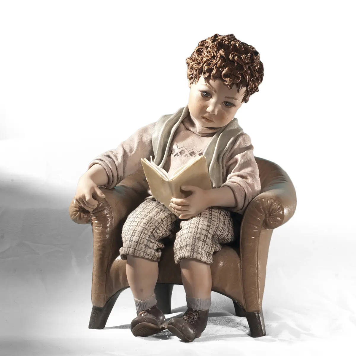 Statua in porcellana di Sibania con bimbo seduto su poltrona, maglioncino salmone a rombi e libro di poesie aperto sulle gambe.