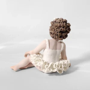 Statua in porcellana di bimba ballerina in tut&ugrave; di pizzo, seduta a terra di lato con fiocco bianco tra i capelli.