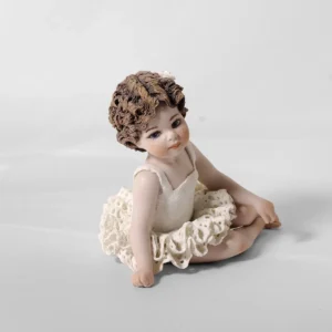 Statua in porcellana di bimba ballerina in tut&ugrave; di pizzo, seduta a terra con le gambe di lato e fiocco bianco.