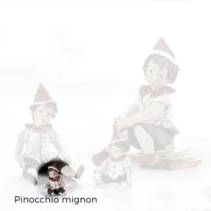 Pinocchio mignon in porcellana seduto a terra, casacca bianca a pois rossi, pantaloni neri e cappello a punta rosso.