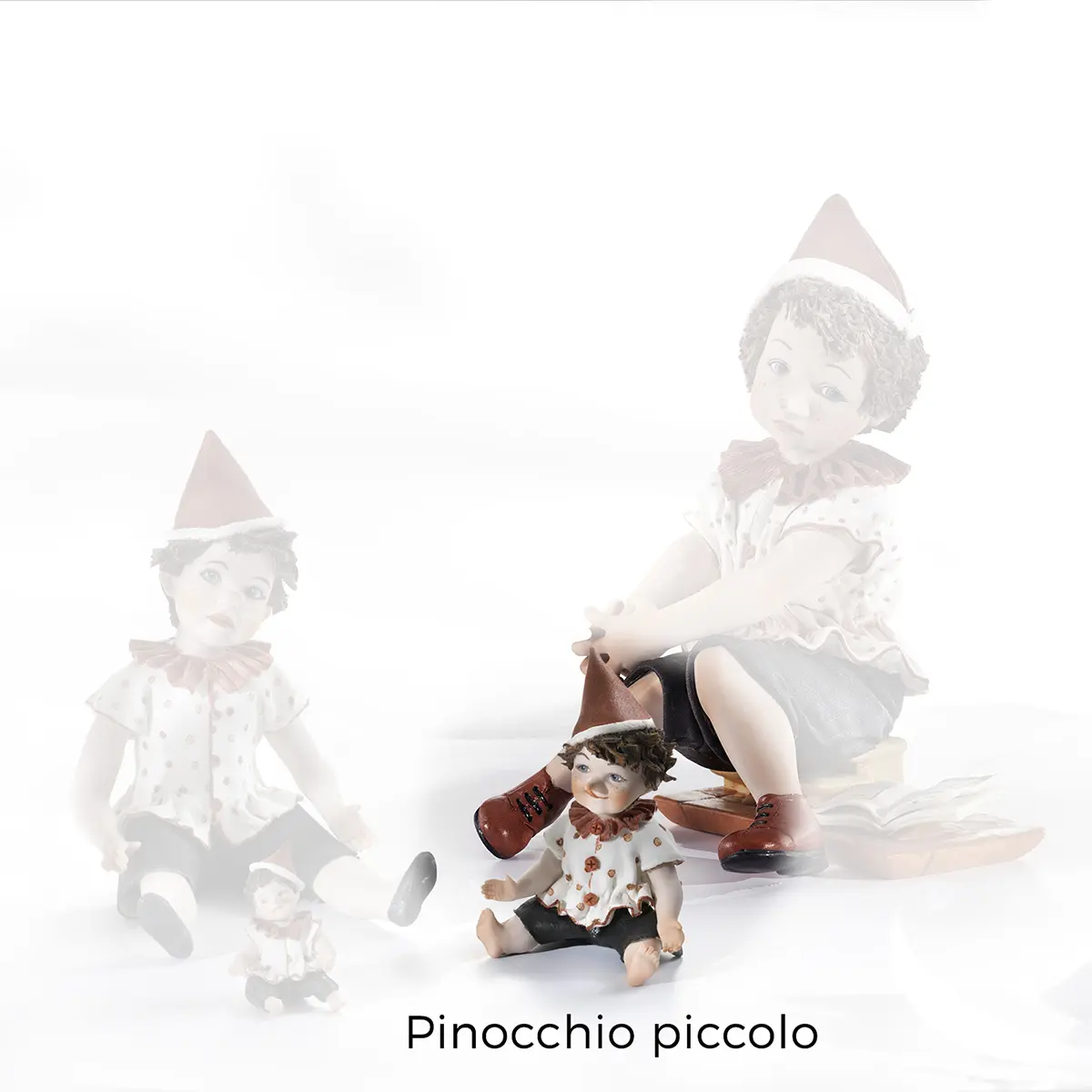 Figura in porcellana di Pinocchio seduto a terra, con casacca bianca a pois rossi e cappello a punta rosso.
