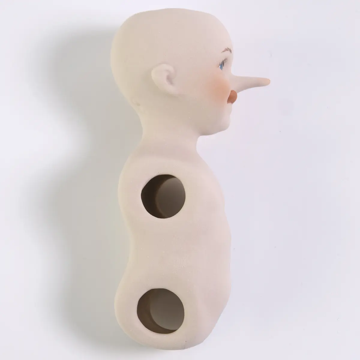 Bambolina in porcellana biscuit di Pinocchio birichino con la linguetta di fuori e il naso lungo.