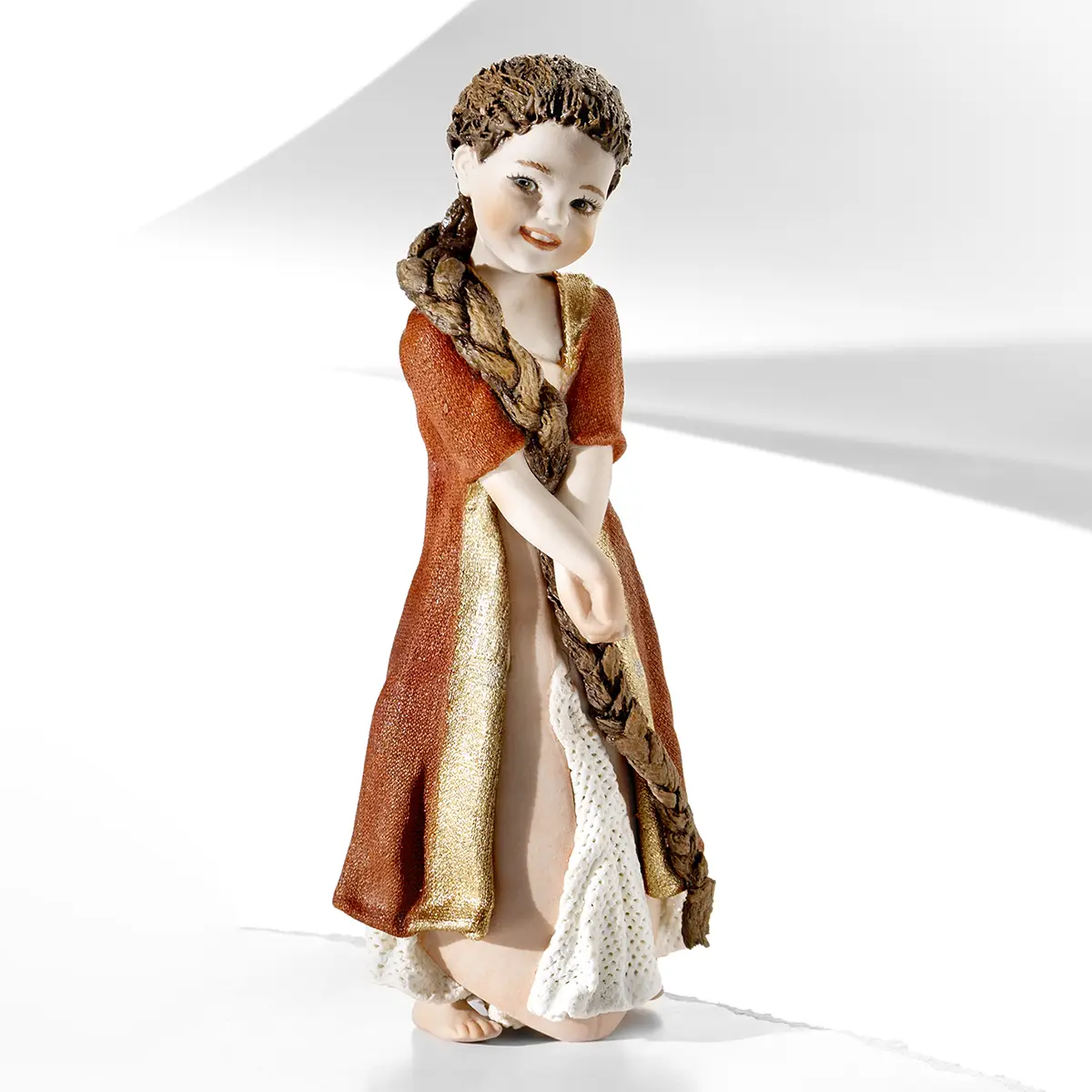 Statua in porcellana di Raperonzolo con abito rosa, giacca rossa con bordi dorati e treccia di capelli su una spalla.