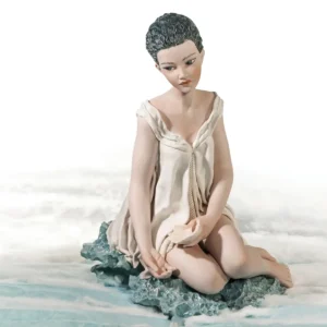 Statua in porcellana di un'ondina con abito bianco, seduta su un'onda turchese e con una conchiglia in mano.