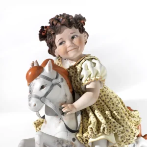 Statua in porcellana con bimba su cavallino a dondolo, abito giallo a fiorellini e capelli in due codine alte.